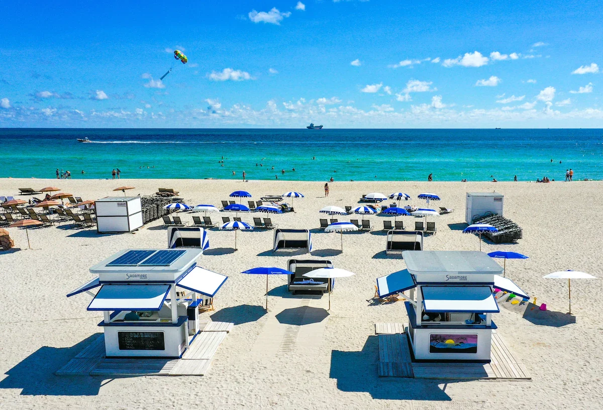 The Sagamore beach cabanas and blue and white umbrellas on the sand, with the ocean behind